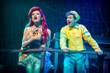 A person with long red hair singing with a man in a yellow sailor's costume