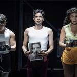 A Chorus Line Production shot.(L-R) Archie Durrant (Mark Anthony), Manuel Pacific (Paul San Marco) and Jocasta Almgill (Diana Morales) They are all holding print-outs of their black and white headshots in their hands. Archie and Jocasta are looking down thoughtfully and Manuel is looking up, speaking to the audience.