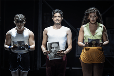 A Chorus Line Production shot.(L-R) Archie Durrant (Mark Anthony), Manuel Pacific (Paul San Marco) and Jocasta Almgill (Diana Morales) They are all holding print-outs of their black and white headshots in their hands. Archie and Jocasta are looking down thoughtfully and Manuel is looking up, speaking to the audience.