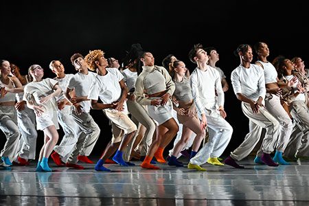 A group of young people dressed in white and various coloured socks dancing on a stage.