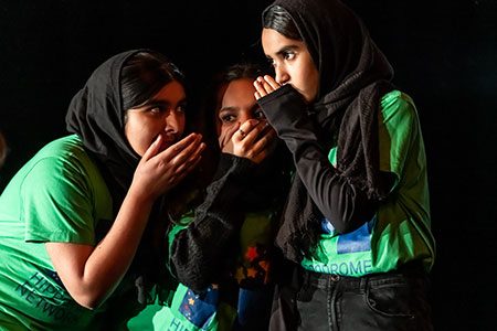 Three girls in headscarves and green t-shirts whispering with each other