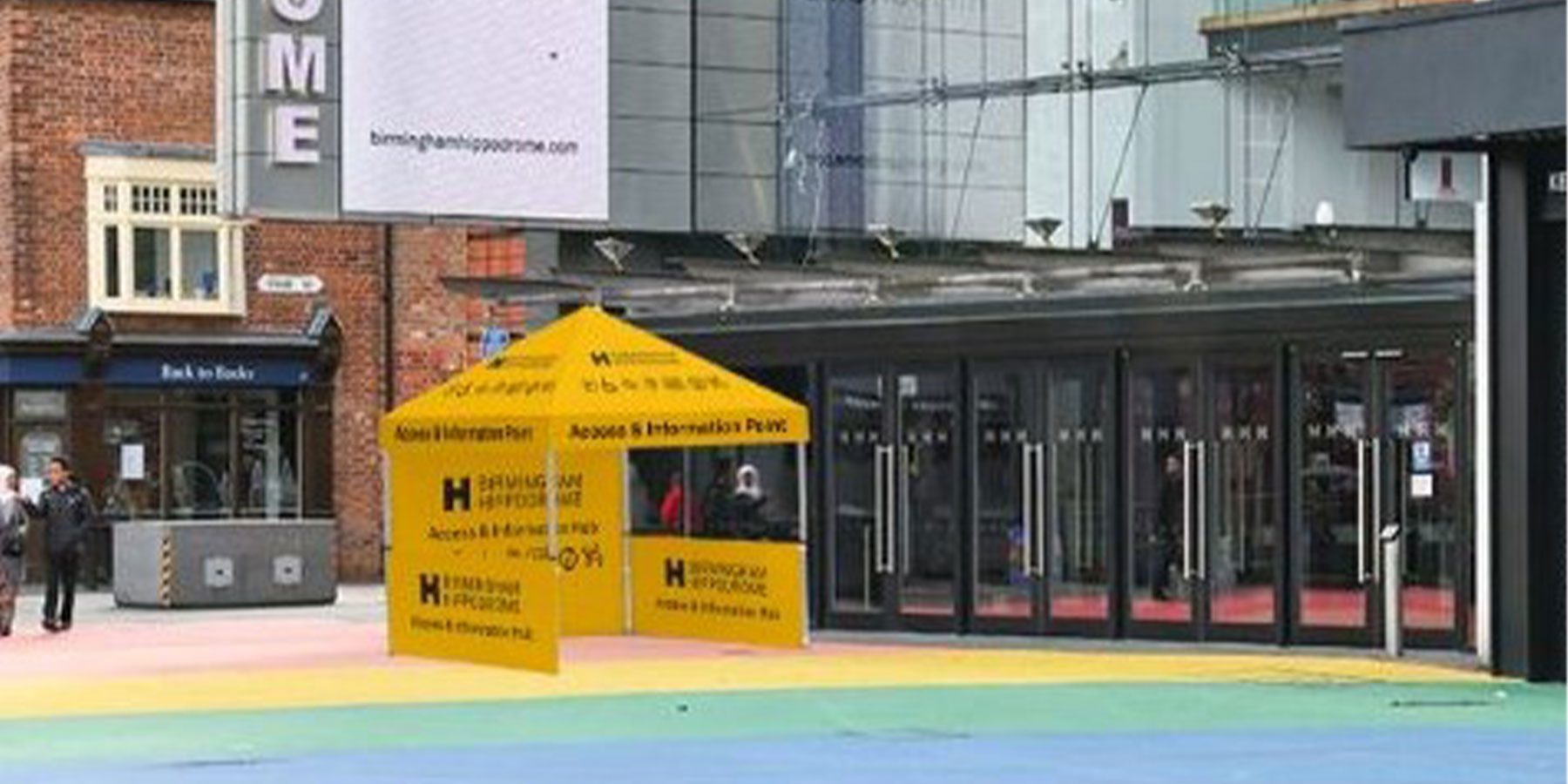 Access & Info Point - Hippodrome Square. Weekender Festival image. A small yellow tent on the rainbow square outside the Hippodrome.