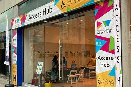 Access Hub outside. Weekender Festival image. The façade of the Access Hub near the East entrance to the Bullring. It has a colourful border around the front and two big glass doors.