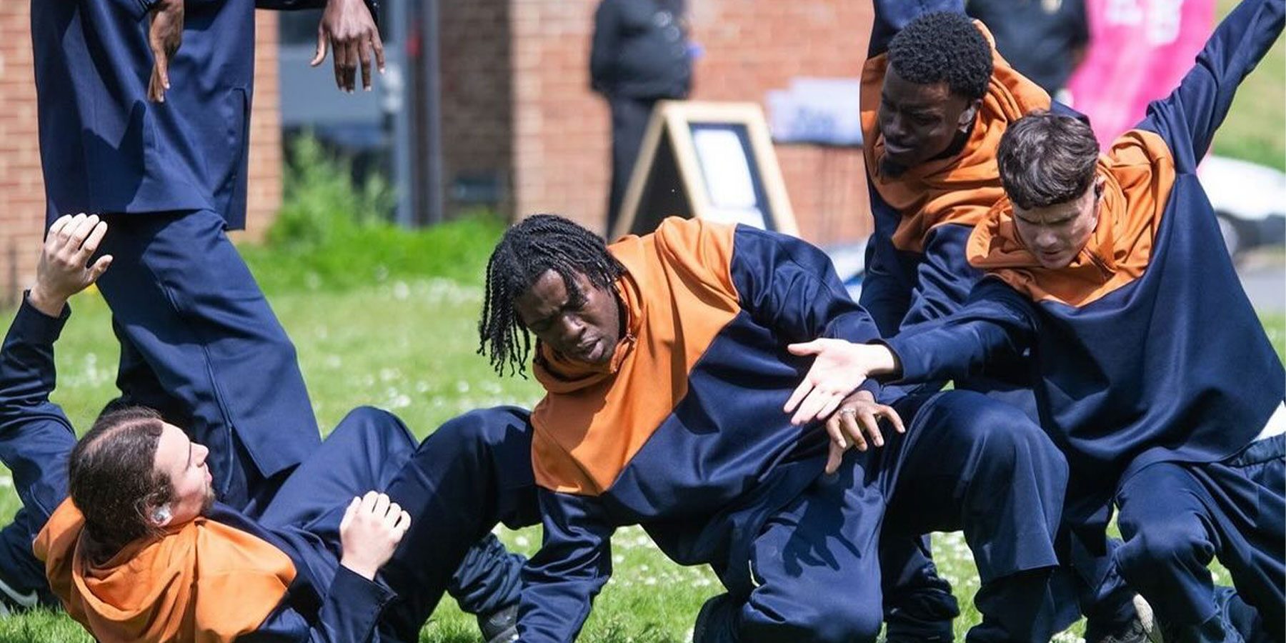 Closer to my dreams Weekender image. Four young dancers wearing orange and blue jumpers are leaning towards the floor, they look like they are all reaching for something far away.