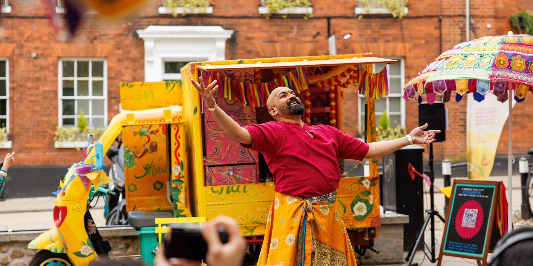 Teabreak Weekender image. A man stands in front of a brightly coloured Tuk-tuk, smiling and holding his arms out wide.