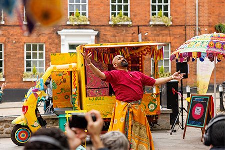 Teabreak Weekender image. A man stands in front of a brightly coloured Tuk-tuk, smiling and holding his arms out wide.