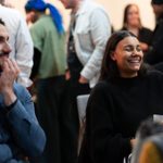 Two people sitting and taking part in larger group event.