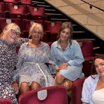 Group of people sit in theatre seats, smiling happily at camera.