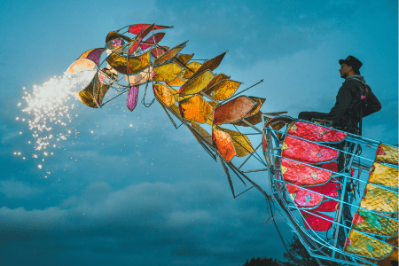 Colourful puppet-like dragon blows glowing sparkles from its mouth.