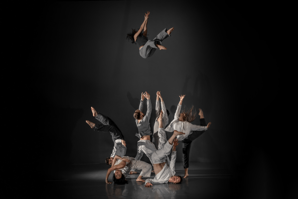 Dancers dressed in grey reaching up with one dancer falling from the sky