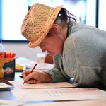 Person with sparkly hat sits writing at a table.