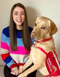 Advocate Sophie Jackson, wearing a multi-coloured, striped jumper, sits smiling with her dog