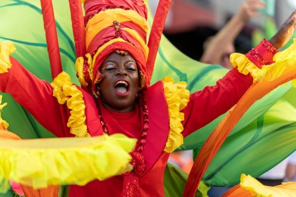 Performer in vibrantly coloured carnival costume performs in public space.