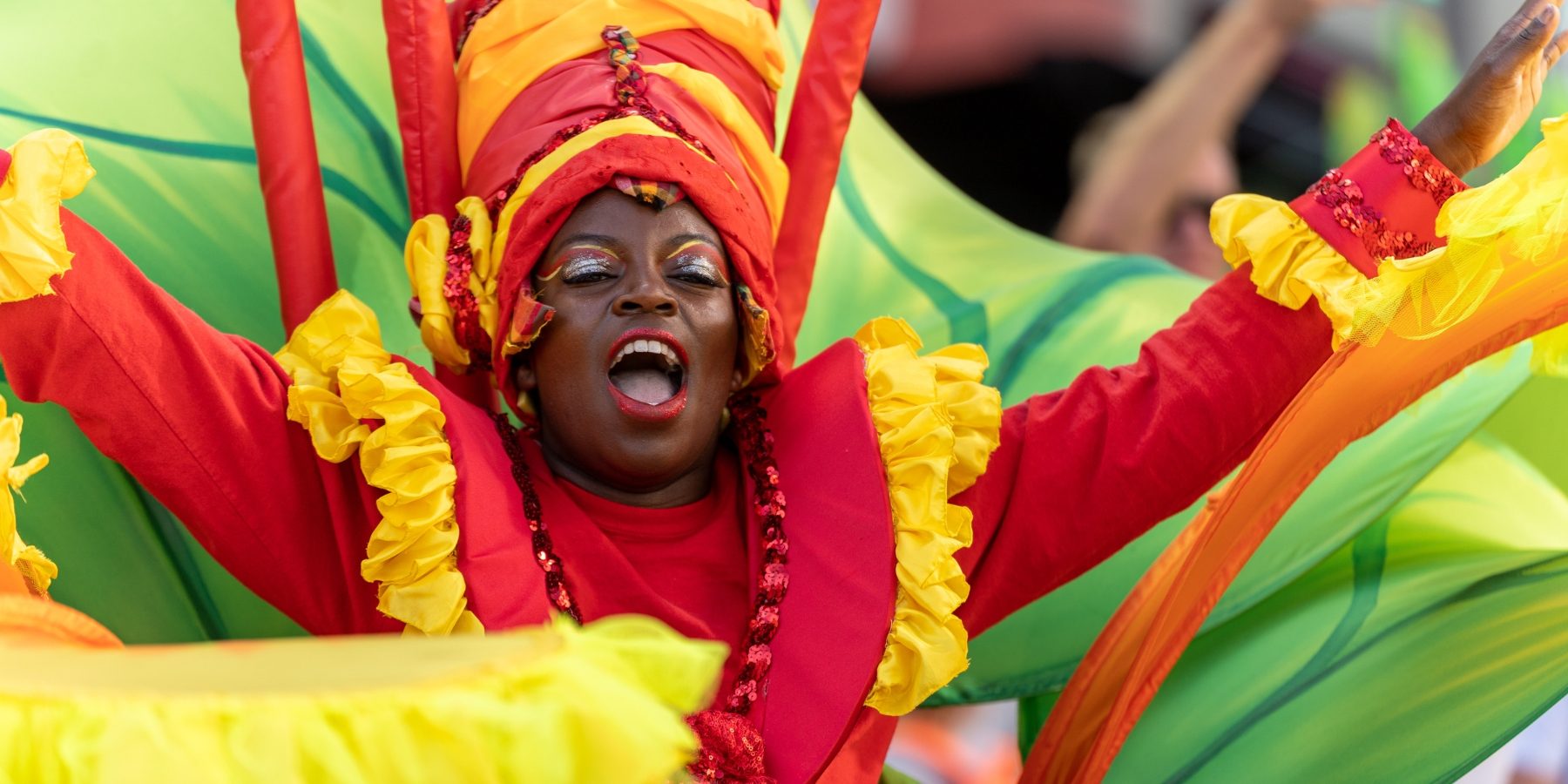 Performer in vibrantly coloured carnival costume performs in public space.