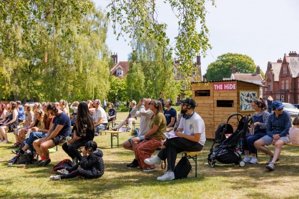 People sitting on chair in a green, outdoor area watching a performance.