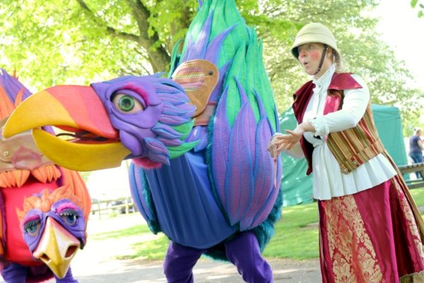 A large colourful bird-like puppet being moved by a performer wearing an explorer's outfit.