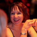 Person sits smiling at someone else at a table.